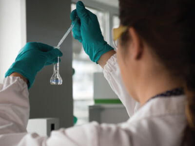 A scientist holds a pipette and small vial containing water as she does a system optimization analysis